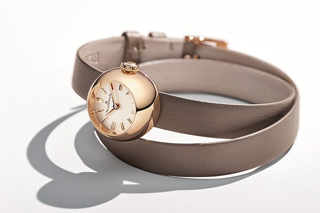 A small spherical red gold watch on a long taupe double-wrap leather strap